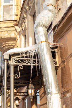 Keskin buz saçakları ve çatının çatısından sarkan erimiş kar. Dikey fotoğraf.