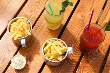 İki kase patates kızartması, kremalı sos ve ahşap masada iki limonata. Açık hava kafe, güneşli bir günde kahvaltı. Fast food, düz yat..