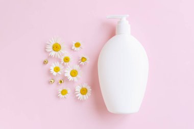 Beyaz pompa nemlendirici krem ya da sıvı sabun şişesi ve pembe arka planda papatya çiçeği. Model, ön üst manzara, yakın çekim. Ürün markalaştırma, el kremi, duş jeli. Düz yatıyordu