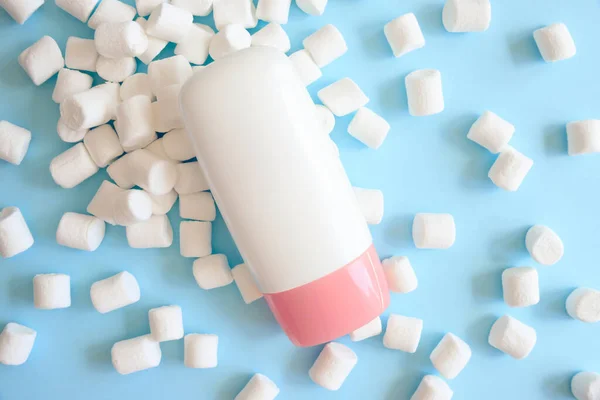 Mockup white cosmetic tube bottle with pink screw cap and white mini marshmallows on blue background. Moisturizing cream, shower gel, skin care, sunscreen, moisturizer, make up, front view, mock-up.