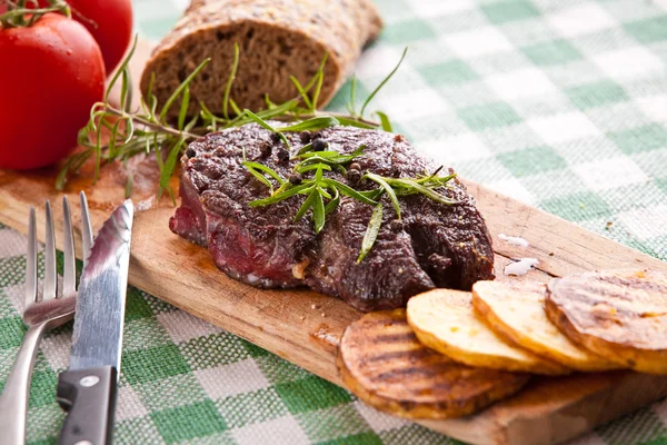 Bife grelhado, batatas assadas e legumes em pão de madeira — Fotografia de Stock