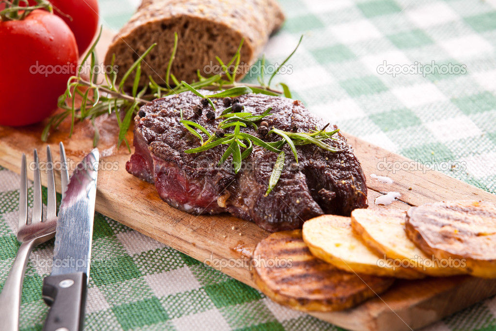 Grilled beef steak, baked potatoes and vegetable on wooden bread
