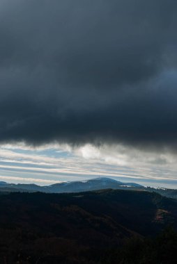 Dağlık arazi, bulutlu bir gün batımı gökyüzü, fırtınalı hava, dağlar yeşil ve turuncu renklerle ağaçlandırılmış..