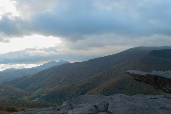 Dağlık arazi, bulutlu bir gün batımı gökyüzü, fırtınalı hava, dağlar yeşil ve turuncu renklerle ağaçlandırılmış..
