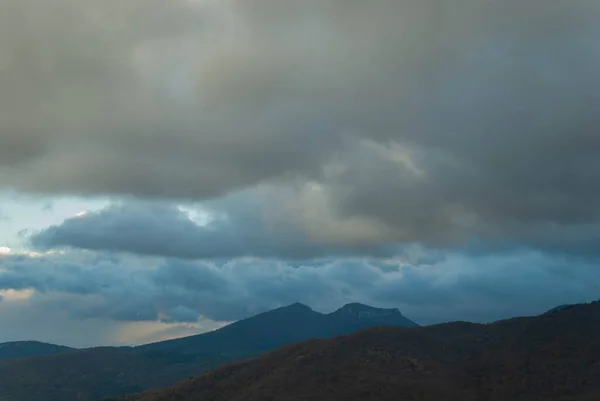 Dağlık arazi, bulutlu bir gün batımı gökyüzü, fırtınalı hava, dağlar yeşil ve turuncu renklerle ağaçlandırılmış..