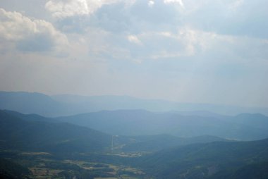 Dağlık yeşil dağ sıraları, açık mavi gökyüzü ve birkaç bulutla kaplı..