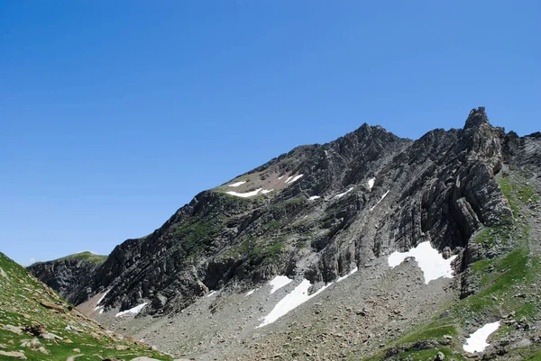 Dağlık yeşil dağ sıraları, açık mavi gökyüzü ve birkaç bulutla kaplı..