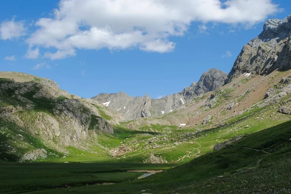 Dağlık yeşil dağ sıraları, açık mavi gökyüzü ve birkaç bulutla kaplı..