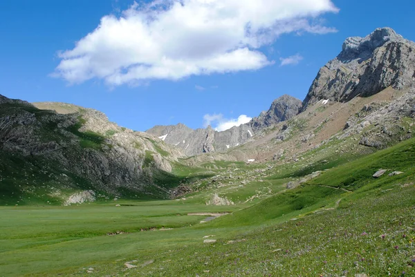 Dağlık yeşil dağ sıraları, açık mavi gökyüzü ve birkaç bulutla kaplı..