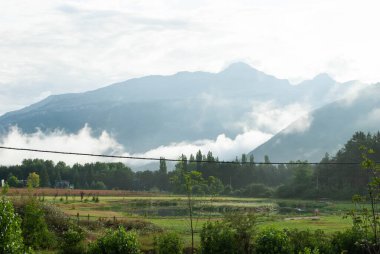 Arka planda dağlarla çevrili, bulutlar içinden geçiyor.