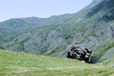 Dağlarla çevrili yeşil vadi ve bulutlu açık mavi bir gökyüzü.