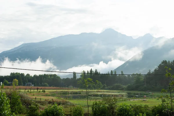Arka planda dağlarla çevrili, bulutlar içinden geçiyor.