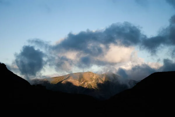 Güneşin doğuşu ya da batışı yüksek dağlarda, yeşil bir vadide ve bulutlu açık bir gökyüzünde