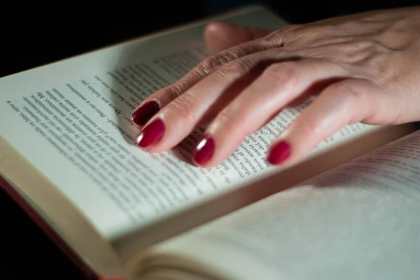 Yaşlı bir kadının okuduğu bir kitabı tutan eller parmaklarını kelimelerle dolu satırlarda kullanır.