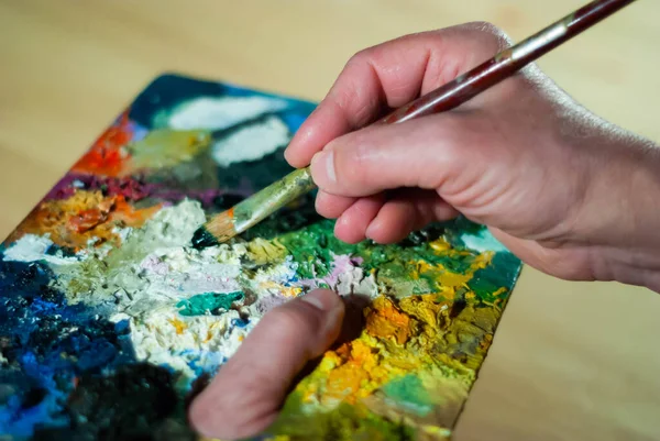 Painter\'s hands taking a paint brush from his palette to paint an oil painting