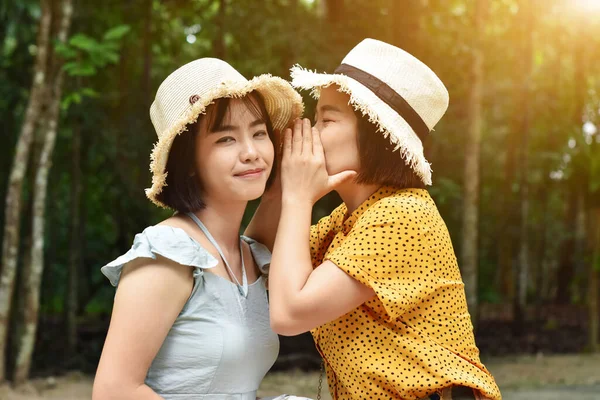 帽子の中に身を包んだ2人のアジアの女の子のクローズアップは 屋外で公園で秘密の耳をささやく織り — ストック写真