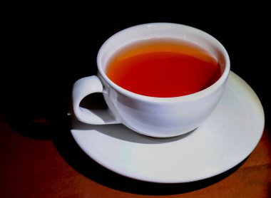 Ferahlatıcı bir fincan siyah çay, yumuşak ışıklandırma, koyu ahşap zemin.