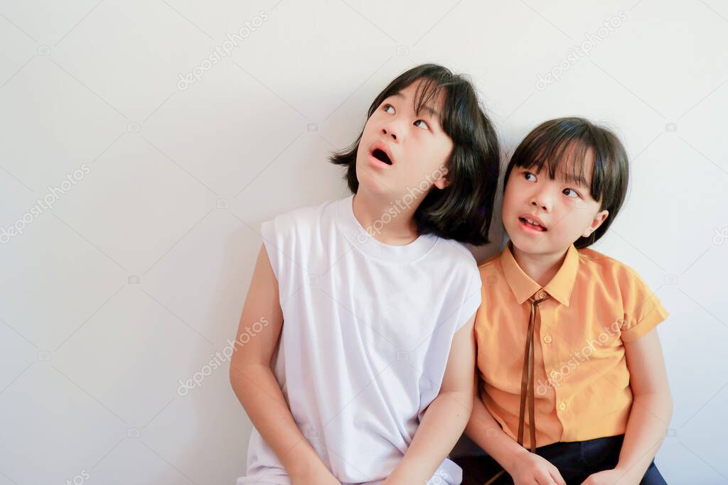Two girls sit close up, looking up, showing different faces on whitewash background.