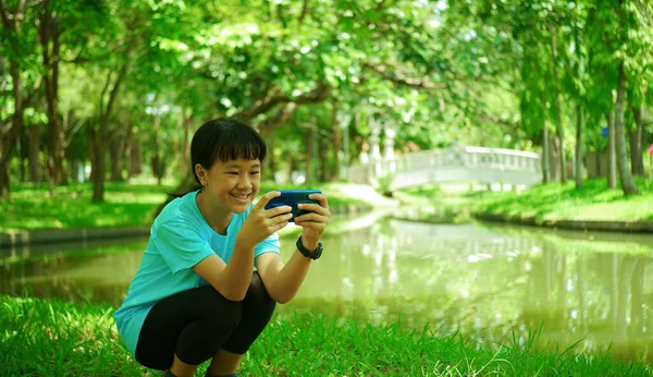 公園で携帯電話に座っているアジアの少女の背景画像 — ストック写真