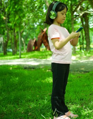 Parkta rahat bir şekilde müzik dinleyen Asyalı bir kız.