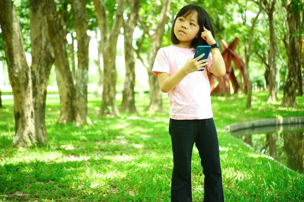 女の子は電話で遊んで自然公園の背景で楽しみを持っています — ストック写真
