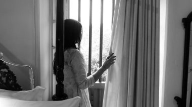 Kolkata, Hindistan, tarih 03.12.2021. Pencere perdesi deliğinden dışarı bakan bir kadının siyah ve beyaz görüntüsü..