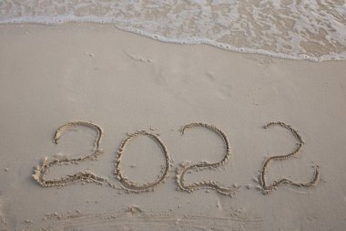 Rakamlar 2022 plajın beyaz kumları ve köpüklü deniz dalgalarıyla yazılmış. Sıcak ülkelerde yeni yılı kutluyoruz. Yeni yıl ve seyahat içeriği.