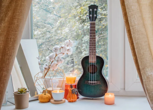 Sonbahar kompozisyonu mumlar, ayna, çiçekler, balkabağı heykelcikleri ve kızların odasındaki pencere eşiğinde ukulele. Tatil için ev dekorasyonu, Şükran Günü, Cadılar Bayramı, doğum günü. Rahatlık ve sükunet