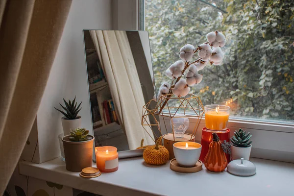Autumn composition of candles, mirror, flowers and pumpkin figurines by the window in girl\'s room. Home decoration for holidays, Thanksgiving, Halloween, birthday. Modern design