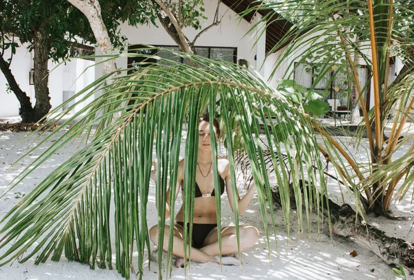 ビキニの女の子がヤシの下のハスの位置に瞑想エキゾチックな熱帯の島のビーチに残します 健康的なライフスタイル 精神衛生だ 旅行コンテンツ — ストック写真