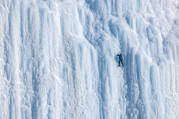 The ice climber climbs the vertical wall. Athletes enjoy the outdoors by climbing the ice wall. Active people enjoying adrenalin sports.