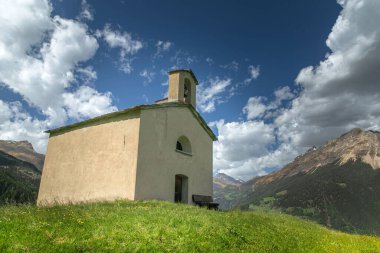 Alplerin arasındaki dağın tepesinde eski bir kilise. İsviçre, Grisonlar Kantonu. Poschiavo 'da. Bahar çiçekli alp çayırları