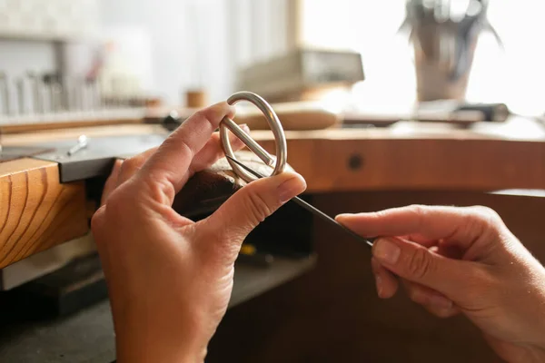 Handmade. Making elements for a leather belt with your own hands. Machining a metal buckle with a file and a hammer in a workshop.