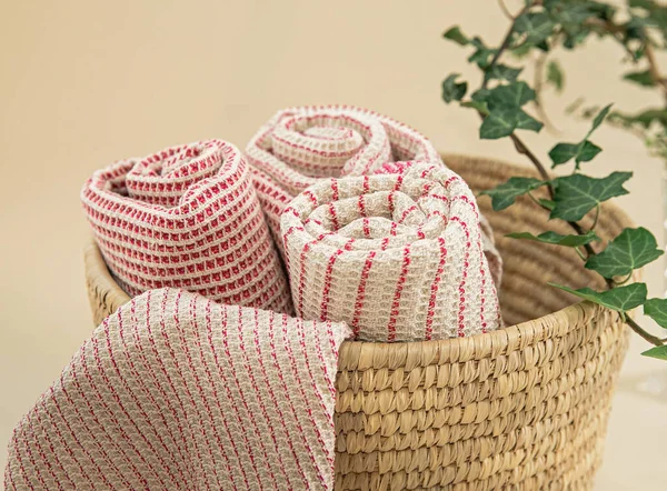 Towels made of natural materials in a wicker basket on a uniform background. Handmade. natural muslin kitchen towels. Natural, soft, airy and stylish kitchen textiles.