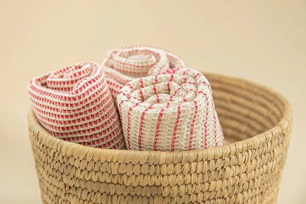 Towels made of natural materials in a wicker basket on a uniform background. Handmade. natural muslin kitchen towels. Natural, soft, airy and stylish kitchen textiles.