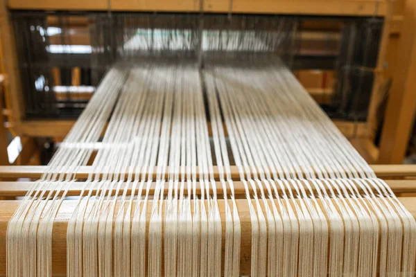 close up of weaving machine. A loom machine for clothing or woven label. Weaving machine for garment industry. Yarn thread lines on the weaving loom machine for clothing in textile factory.