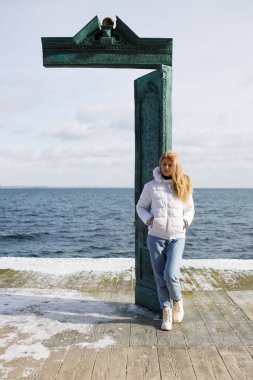 Beyaz ceketli ve kot pantolonlu kadın Odessa plajı Lanzheron 'da antik kapının yanında, Nemo Dolphinarium yakınlarında, sanat objesi. Heykelin adı 