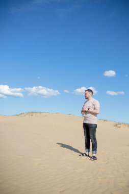 Çölde kum tepesinin tepesinde otururken elinde şişe suyla duran yorgun genç adam, etrafta kum ve biraz yeşillik var. Sıcak yaz havası, gezegeni dolaşma kavramı. Avro Çölü