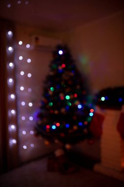 Yılbaşı ağacı ve akşam süslenmiş bir ev. Hediye kutuları ve beyaz tuğlalı şöminenin yanında kırmızı çoraplar. Konsept - Önümüzdeki 2022 Yeni Yıl. Sakin ve huzurlu bir atmosfer. Kasıtlı olarak bulanık