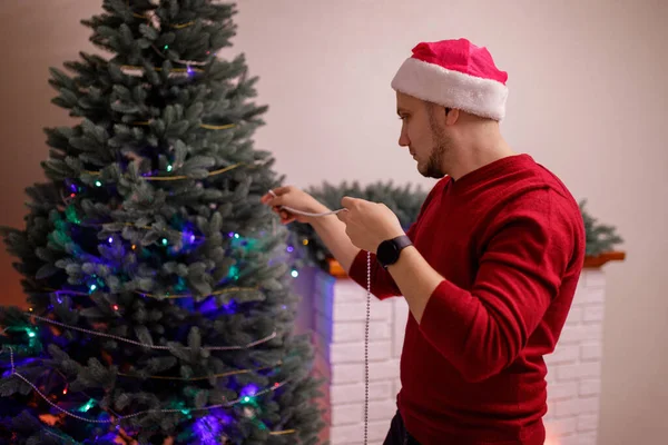 Fiatal Férfi Piros Pulóverben Santa Hat Díszíti Golyókat Játékokat Tüzek — Stock Fotó