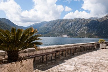 Perast, Karadağ - 15.09.2021: Roma Katolik Kilisesi dağ sıraları ve mavi gökyüzünün önündeki boka kotor körfezindeki kayalıklardaki leydimiz. Unesco 'nun dünya mirası. Burada palmiyeler yetişir.
