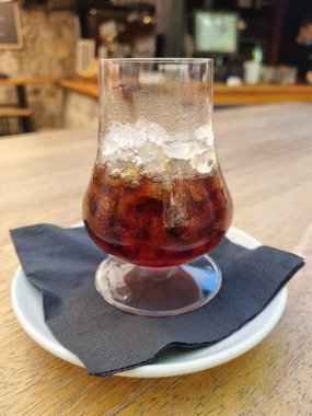 Büyük bardakta buzlu kahve ve viski. Koyu peçete ve beyaz tabakta soğuk yaz içeceği, Kafe 'de açık ahşap masa.