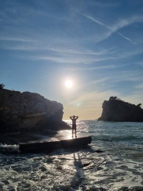 Karadağ 'ın Budva kentindeki Saint Nikola Adası' ndaki (Hawaii) kayalıkların yanındaki sahilde bir adam duruyor. Cennet Sahili 