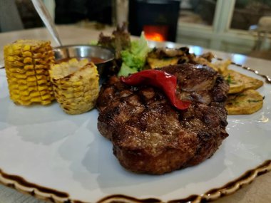 Tahta masada beyaz tabakta servis edilen sebzeli ızgara biftek.