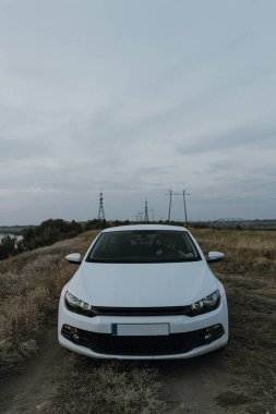 Siyah güneş gözlüklü, beyaz tişörtlü yakışıklı adam modern beyaz spor arabasında oturur ve gün batımını seyreder. Riverside yakınlarında şehir dışında bir hafta sonu. Koyu renkli fotoğraf