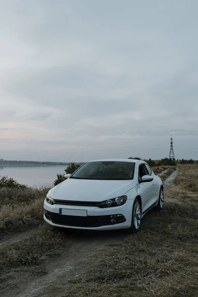 Siyah güneş gözlüklü, beyaz tişörtlü yakışıklı adam modern beyaz spor arabasında oturur ve gün batımını seyreder. Riverside yakınlarında şehir dışında bir hafta sonu. Koyu renkli fotoğraf