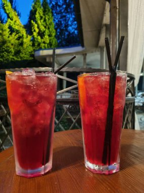 Gece kulübündeki ahşap bir masada buzlu bardakta kırmızı kokteyl.