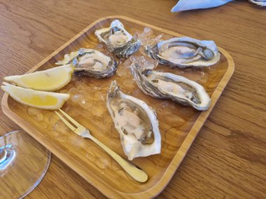 İstiridye deniz ürünlerini test etmek, ahşap bir masada bir bardak beyaz şarapla, nehir manzaralı bir restoranın dışında.,  