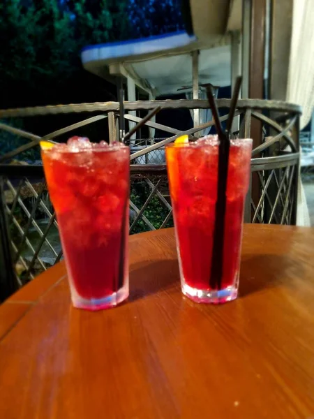 Gece kulübündeki ahşap bir masada buzlu bardakta kırmızı kokteyl.