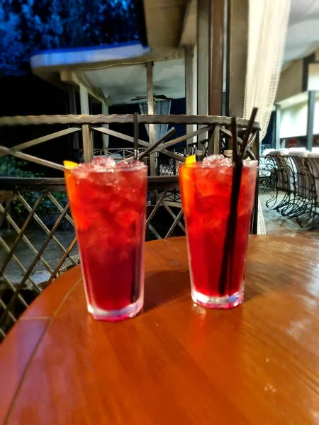 Gece kulübündeki ahşap bir masada buzlu bardakta kırmızı kokteyl.